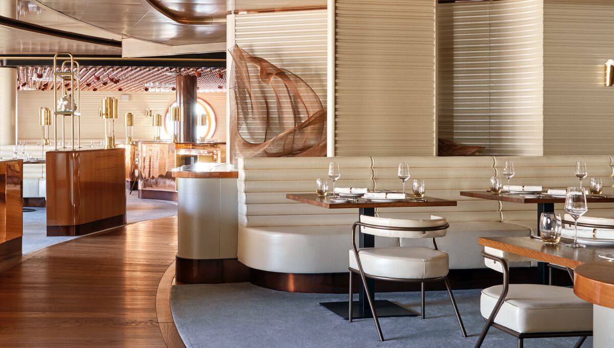 The Wake restaurant aboard a Virgin Voyages ship, with curved banquettes, warm wood and a sweeping staircase