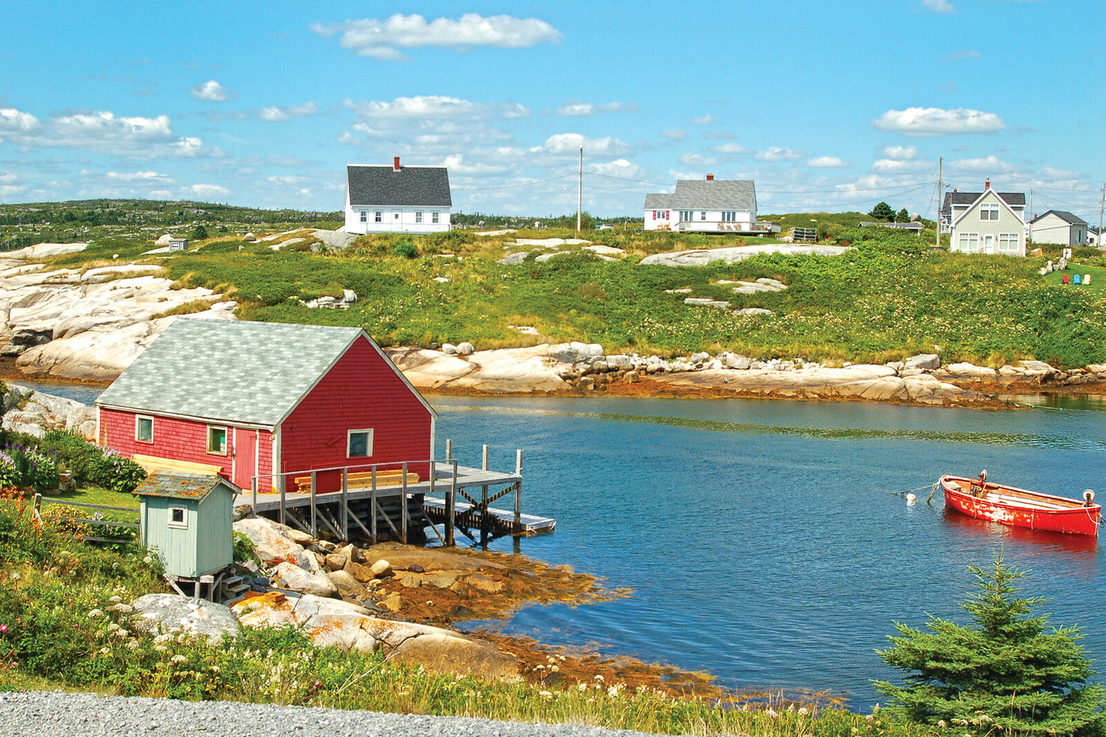 A red boathouse and skiff sit among granite boulders and cottages around the protected cove at Peggy's Cove, Nova Scotia